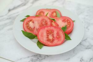 Tomato slices with basil leaves on a white plate. Selective focus. photo