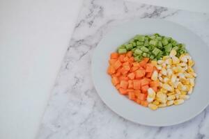 Frozen vegetables on a white plate on a white marble table. photo