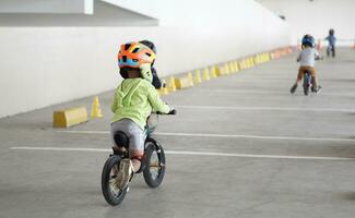 kids from 3 years old races on balance bike in a parking area with cones as track, back view, behind view shoot. photo