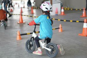 young girls 5 years old races on balance bike in a parking area with cones as track, back view, behind view shoot. photo