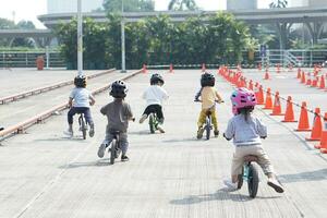 kids from 2-5 years old races on balance bike in a parking area with cones as track, back view, behind view shoot. photo