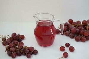 uva jugo en un vaso jarra con Fresco uvas en un blanco antecedentes foto