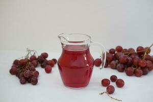 uva jugo en un vaso jarra con Fresco uvas en un blanco antecedentes foto