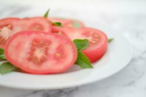 Tomato slices with basil leaves on a white plate. Selective focus. photo