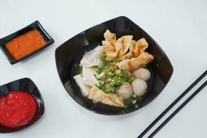 a bowl of meatball soup with chopsticks and chili sauce photo