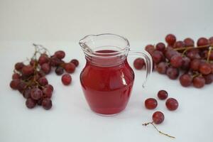 uva jugo en un vaso jarra con Fresco uvas en un blanco antecedentes foto