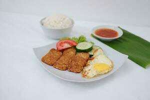 Fried tempeh cutlet with rice and fried egg on white plate photo