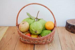 cesta de manzanas, naranjas y guayaba en un de madera mesa, valores foto