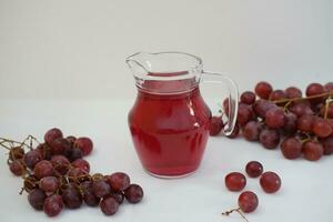 uva jugo en un vaso jarra con Fresco uvas en un blanco antecedentes foto