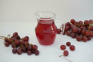 uva jugo en un vaso jarra con Fresco uvas en un blanco antecedentes foto