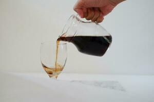 Pouring cola from a jug into a glass on a white background photo