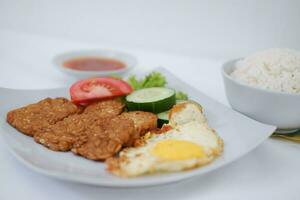 Fried tempeh cutlet with rice and fried egg on white plate photo