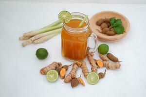 Fresco jengibre y limón jugo en un vaso tarro con jengibre raíces en blanco antecedentes. foto