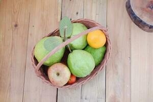 Basket of apples, oranges and guava on a wooden table, stock photo