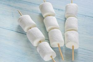 Marshmallow skewers on the wooden background photo