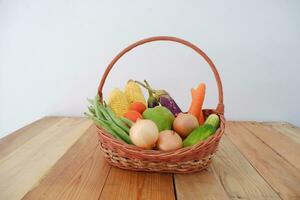 Vegetables in a basket on wooden background. Healthy food concept. photo