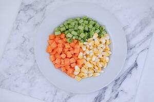 congelado vegetales en un blanco plato en un blanco mármol mesa. foto