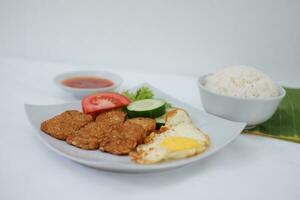 Fried tempeh cutlet with rice and fried egg on white plate photo