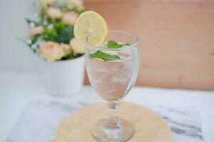 vaso de agua con limón y menta en un de madera mesa, valores foto