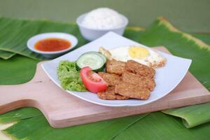 Fried tempeh cutlet with rice and fried egg on white plate photo