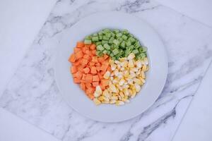 congelado vegetales en un blanco plato en un blanco mármol mesa. foto