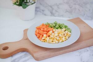 congelado vegetales en un blanco plato en un blanco mármol mesa. foto