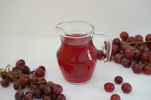 uva jugo en un vaso jarra con Fresco uvas en un blanco antecedentes foto