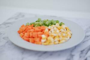 congelado vegetales en un blanco plato en un blanco mármol mesa. foto