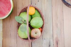 Basket of apples, oranges, guava and watermelon on a wooden table, stock photo