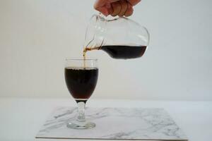 Pouring cola from a jug into a glass on a white background photo