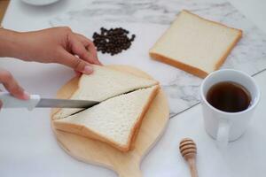 Woman cutting bread with knife and cup of coffee on white table. photo