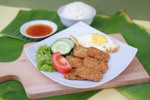 Fried tempeh cutlet with rice and fried egg on white plate photo