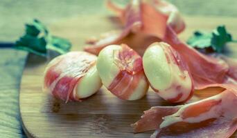 Mini cheese and prosciutto wraps on the wooden board photo