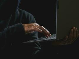 Hacker spy man one person in black hoodie sitting on a table looking computer laptop used login password attack security to circulate data digital in internet network system, night dark background. photo