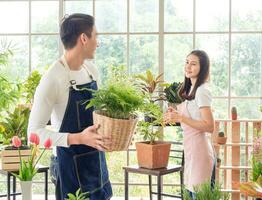 Gardener young Asian man woman two person family stand  smiling lookand helping organize small tree. Inside room  tree leaf green in calm work shop home plant . hobby job happy and care concept photo