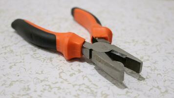 Pliers with black and orange handles on a white floor photo