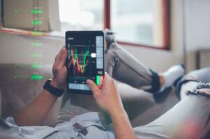 businessman sitting on couch at home holding smartphone with virtual trading graph, using cell phone mobile apps, Social media influence concept photo