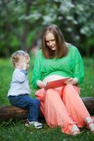 Pregnant mother with little son using touch pad in the park photo