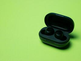 negro inalámbrico auriculares con el cargando caso en un verde antecedentes. foto