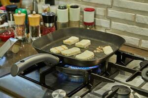 Halloumi cheese is fried on ribbed pan over fire on gas stove photo