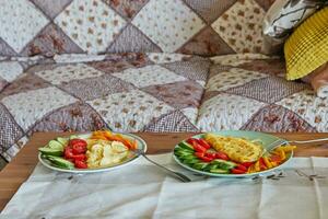 Morning healthy breakfast of scrambled eggs with parmesan cheese, cucumbers, cherry tomatoes and sweet peppers on the coffee table in front of the sofa photo