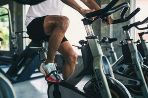 cerca arriba piernas de asiático deportista hacer ejercicio en un bicicleta en el gimnasia, determinación a cardio perder peso, hace su saludable. ejercicio bicicleta hombre aptitud deporte concepto. foto