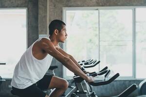 deportista asiático haciendo ejercicio en bicicleta en el gimnasio, la determinación de hacer cardio perder peso, la hace saludable. concepto de deporte de fitness de hombre de bicicleta de ejercicio. foto