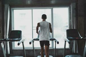 Back side of asian sportman runner running on treadmill in fitness club. Cardio workout. Healthy lifestyle, guy training in gym. Sport running concept. photo