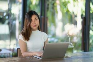 Asian young woman in smart casual wear working on laptop while sitting in creative office or cafe. young girl working with laptop on the wood table in the cafe photo
