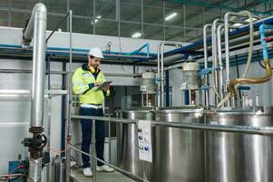 Engineer man in uniform walking to check boiler tanks with liquid pipeline in beverage processing factory photo