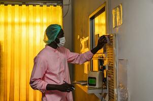 African quality control employee man in sterile suit clock in with time clock system of factory policy before working in processing warehouse photo