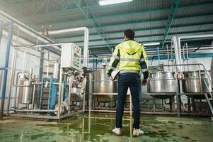 Commitment caucasian technician engineer man in safety uniform standing with pipeline, boiler tank in beverage processing laboratory plant photo