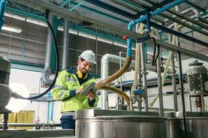 caucásico técnico ingeniero hombre en uniforme con tableta comprobación y controlar caldera tanques y líquido tubería en producción línea a fábrica foto