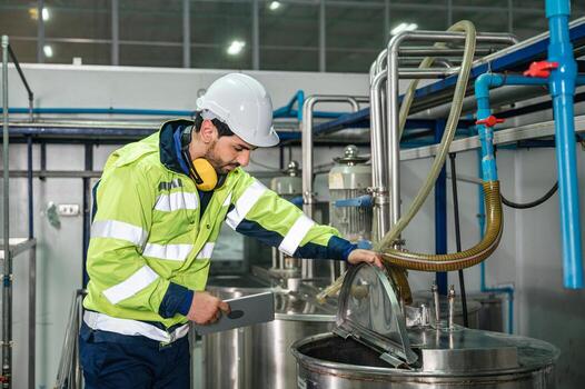 Caucasian technician engineer man in uniform with tablet checking and control boiler tanks and liquid pipeline in production line at factory photo